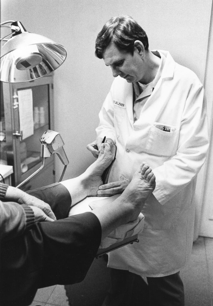 12-1003-008 Print B&W 8x10 LCDR Albert D. Saleker, MSC, USN; Podiatry Clinic, Br. Medical Clinic Bldg. 625 NAS Pensacola, FL - December 1982 [aka Navy podiatrist LCDR Albert Saleker treats a patient at the Branch Medical Clinic, Pensacola, Florida, 1982. Medical Service Corps History Collection Box 20 Podiatry Images